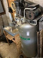 Full side view of gray vertical tank, motor and pump assembly on wooden stand