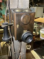 Front angled view showing wooden box phone with two brass bells, mouthpiece, and hanging black receiver on the left.