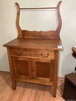 Front view of antique solid wood washstand showing single drawer with metal handles, double panel cabinet doors, with wood towel bar attached.