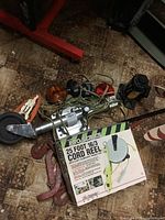 Photo showing a metal trailer jack, a cord reel box with fluorescent light, red magnetic towing lights and tie down straps on the floor.