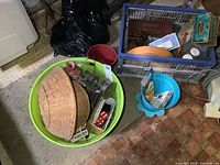 Wide view of lot showing green plastic bin with wicker baskets, glass vases, sewing items and tins scattered inside.