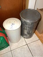 Shows both metal storage bins side by side on the floor against a wooden door.