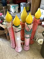 Five tall blow mold candles, three pink and two orange, with yellow plastic flames, displayed together in a storage area.