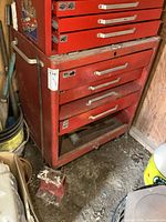 Front view of red Mastercraft bottom tool cabinet with drawers, showing lock bar and drawer handles. Cabinet on wheels, placed in workshop with other items around.