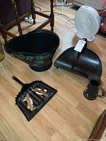 All four items on floor: ash bucket with green ivy decoration, log holder, dustpan with painted rabbits and text, and small metal pitcher