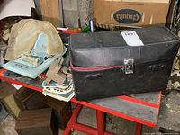 View of all items including the black camera case, blue Paymaster cheque writer, and View-Master with reels on red metal table.