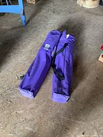 Two purple carrying bags for folding chairs resting on floor, showing size and color.