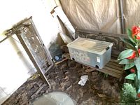 Full view of the second bench side showing cast iron leg and side with broken leg taped, plastic bin with cushions on third bench