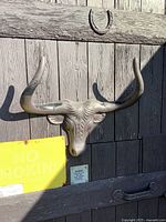 Front view of cast iron steer head mounted on wooden wall, showing full horn span and painted surface.