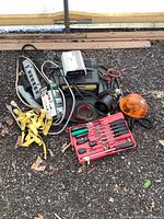 Overview of the lot showing tools, power inverter, charger, cords, orange warning light, horn, and screwdrivers on gravel ground.