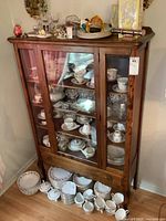 Full view of the china cabinet showing glass doors and wooden frame with interior shelves. Cabinets contain tableware but are not part of the lot.