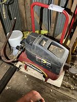 Front view of red Coleman Powermate air compressor with attached hose and black motor housing on top, showing overall condition and setup.