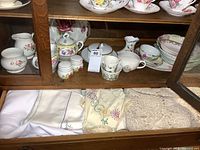 Porcelain cream and sugar sets, gravy boat, bowls and plates with floral motifs inside wooden cupboard with glass door.