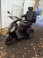 Front-left perspective of black 3-wheel scooter under canopy on gravel