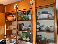 Open cupboards with various kitchen items including glassware, plastic containers, bowls, colander, pitchers.