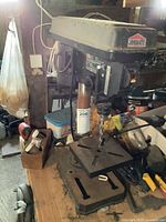 Front-left angle view of Jobmate drill press on wooden workbench with drill bit in chuck, showing overall unit and some surrounding items.