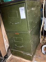 Green metal file cabinet with 2 drawers and a base, showing wear and scratches.