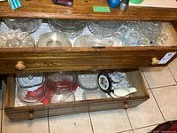 Top and bottom drawers filled with clear glass bakeware, serving dishes, glass lids, juice glasses, bowls, and a porcelain gravy boat.