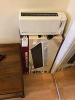 Front view of the white in-line toaster placed on top of the boxed griddle with the box label visible showing the griddle image.