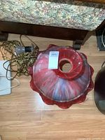 Top view of the slag glass lamp showing the red and white swirled pattern and ruffled edge, with attached brass chain and electrical cord with light bulb socket.