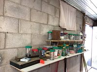 View of shelves with multiple jars containing nails, screws, nuts, bolts, and small hardware items, plus some tools and supplies scattered on the table beneath the shelves.