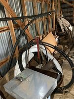 Image showing metal electrical panel box, coiled black hoses, white corrugated ABS pipes, and wooden lumber stacked against corrugated metal shed wall.