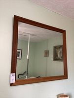 Photo showing entire wooden framed mirror hung on light-colored wall, reflecting a chair and wall art.