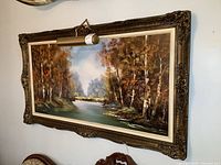 Full view of the framed landscape oil painting with mounted light above on the wall.