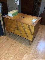 Wooden sewing stand closed showing the exterior with accordion-style sides and tapered legs.