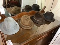 Four men's hats of various colors and materials displayed on a wooden dresser with a mirror, showing overall lot contents