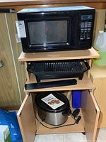 Front and side view of black microwave on wooden shelf with electric grill below and crock pot on lower shelf