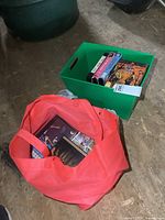 Photo showing red bag and green bin filled with DVDs, VHS tapes, and some CDs arranged on a wooden floor.