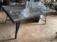Side angle view of patio table showing metal frame, tile top, and various glassware on top.