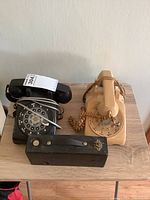 Wide shot of two rotary dial phones (black and beige) and a small black vintage camera on a wooden surface.