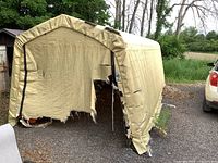 Front view of portable garage showing heavily torn and damaged tan tarp with visible frame inside.