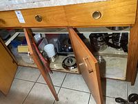 Three open lower kitchen cupboards showing stainless steel pots, pans, and plastic storage containers inside on shelves.