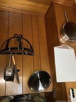 Black metal wall-mounted pot rack and two metal pans hanging on wooden wall paneling