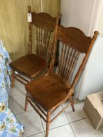 Two solid oak pressback dining chairs with carved upper backrest and turned spindles, showing aged finish and visible wear.