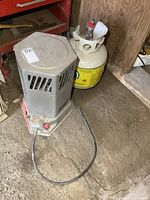 Top-down and side view of Reddy Heater propane heater and attached propane tank positioned on a concrete floor near shelves and wooden walls.