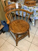 Photo of antique solid wood pub style chair showing front and side angles, placed on tiled floor near table with sunflower tablecloth.