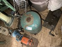 Overview of lot showing blue pressure tank, blue and orange pumps, bench grinder wheels, and other motor components placed on a wooden floor.