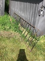 Wrought iron railing leaning on ground outside near metal shed. Shows length, rust, and decorative scrolls.