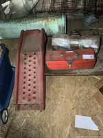 Photo of one red steel automotive ramp beside two metal toolboxes, one red and one silver/grey, showing wear.