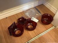 Three red glass lamp shades with scalloped edges and round bases on floor beside wall