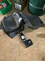 Two black replacement seats and a 24V DC motor on floor; one seat has attached protective skirt, the other is mounted with motor.