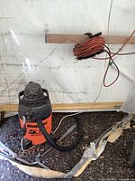 Full view of orange and black 5 gallon Shop-Vac with attached black hose and orange extension cord coiled nearby.