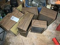 Five untested speakers placed on the floor, three wooden cabinet speakers and two smaller black speakers with grille covers and wires.
