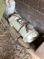 Angled side view of the cream white plastic sprayer tank with red clamp lid and pump showing wear and dirt.