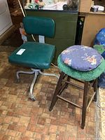 Photo showing vintage metal frame chair with green cushioned seat and backrest beside wooden stool with floral cushion and green cover.