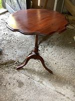 Full view of vintage solid wood tilt top table showing scalloped round top and pedestal base with three legs
